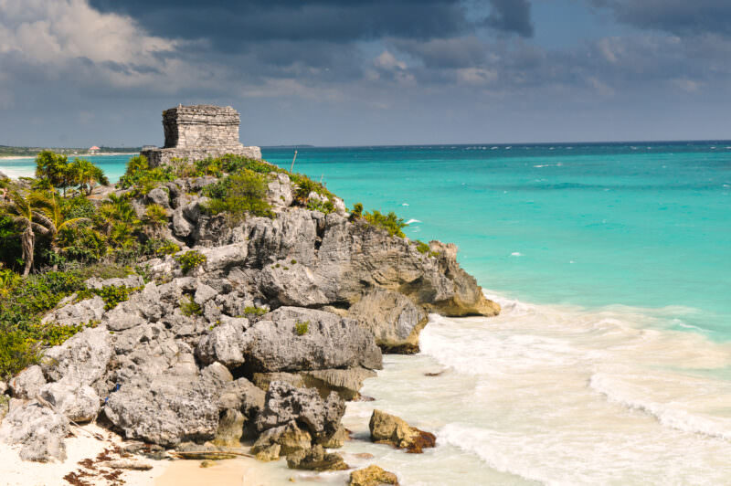 Templo del Dios del Viento at Tulum, a small stone temple atop jagged limestone cliffs above turquoise Caribbean waters