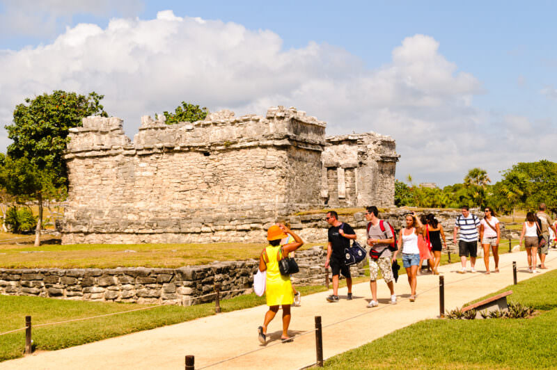 A weathered limestone wall at Tulum, its stacked stone construction and aged surface with visitors walking along a pathway