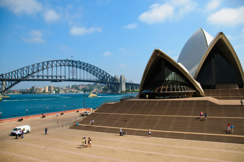 Sydney Opera House rising above monumental steps of Bennelong Point framed by Sydney Harbour Bridge