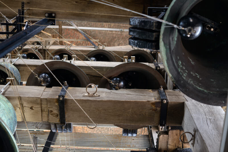 Bronze bells of the Belfry of Bruges carillon, suspended on wooden beams with wire linkages visible in the timber-framed bell chamber