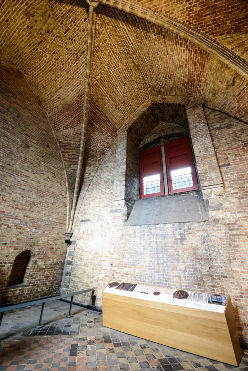 Cross-ribbed brick vault of the Belfry treasury chamber, with arched red-shuttered window and display case on tiled floor