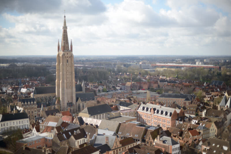 Church of Our Lady spire rising above Bruges rooftops, viewed from the Belfry observation level across the medieval cityscape