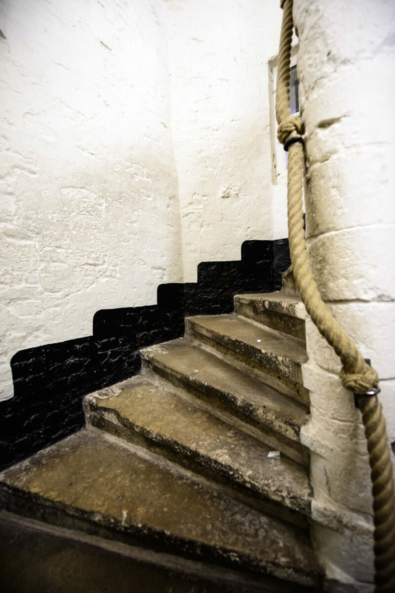 Worn stone spiral staircase inside the Belfry of Bruges, with a rope handrail against whitewashed walls