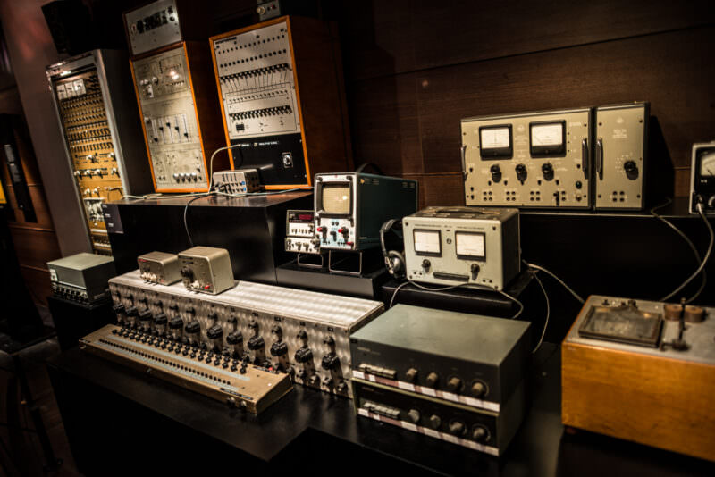 Modular analog synthesizers with patch bays, oscilloscope screens, and rack-mounted units arrayed on gallery platform