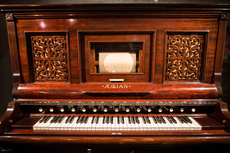Aeolian harmonium circa 1890, burled walnut case with perforated paper roll behind central glass panel, foot treadles below