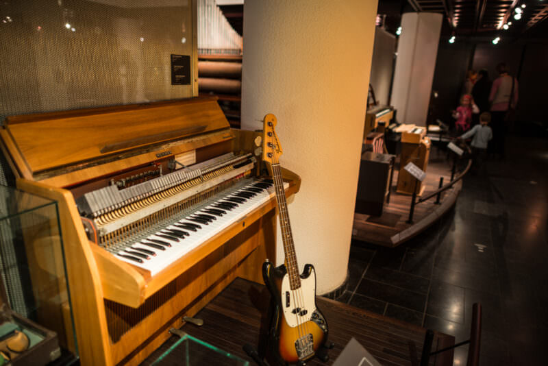Hohner Electra-Piano with exposed hammer action beside Fender Mustang Bass, organ pipes visible in background