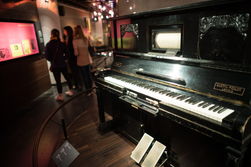 Fiedler pianola circa 1900, perforated paper roll visible in upper window, large foot pedals below black lacquered case