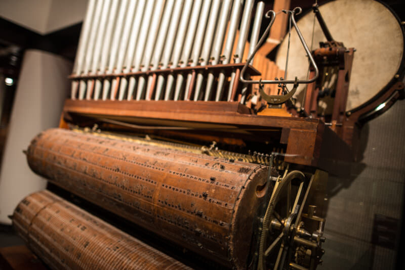 Barrel organ with large wooden pin-studded cylinder, exposed organ pipes, and mechanical percussion elements visible
