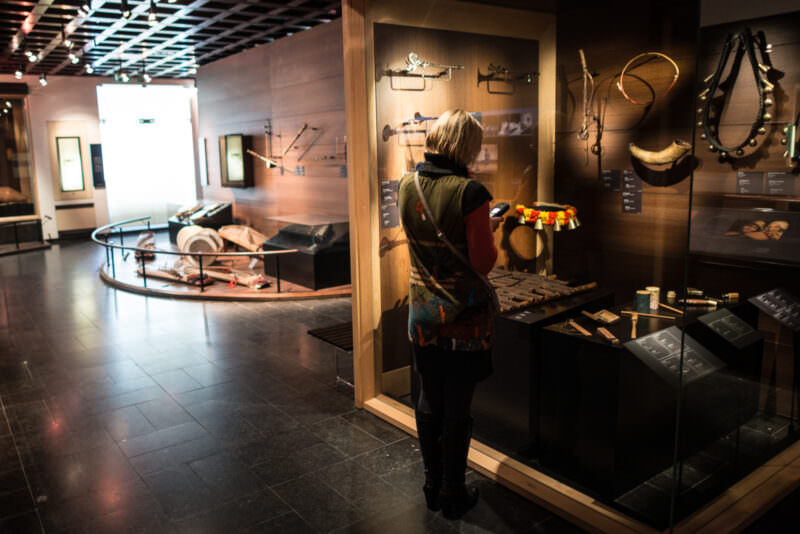 Visitor examining wall-mounted folk instruments including animal-horn wind instruments in darkened museum gallery