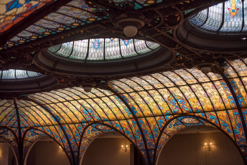 Oval fisheye view of Gran Hotel Ciudad de Mexico atrium showing three circular ceiling medallions and surrounding amber glass panels
