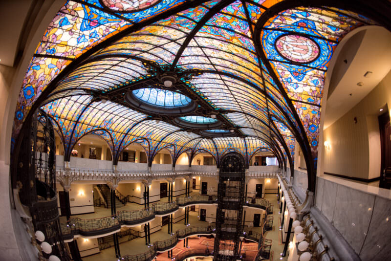 Sweeping view of Gran Hotel Ciudad de Mexico atrium showing curved stained glass vault with floral motifs and wrought-iron balconies