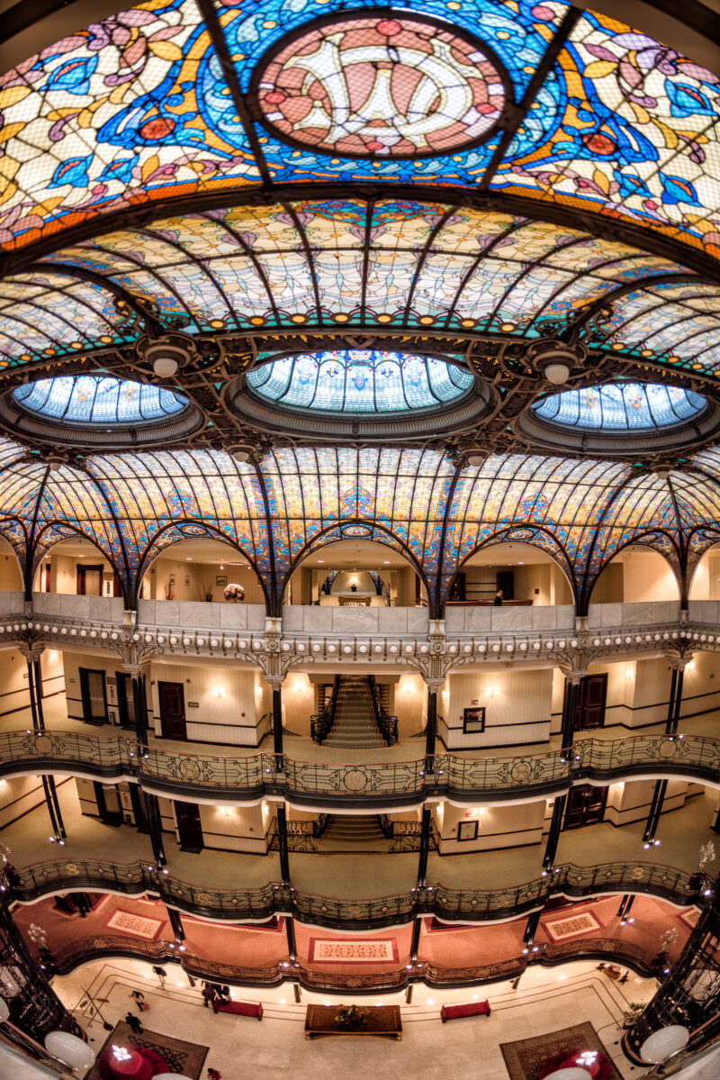 Section of Gran Hotel Ciudad de Mexico ceiling featuring radiating stained glass panels with floral designs and wrought-iron framing
