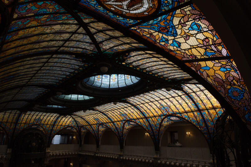 Stained glass ceiling of Gran Hotel Ciudad de Mexico viewed from atrium edge, showing dramatic light and shadow on amber panels