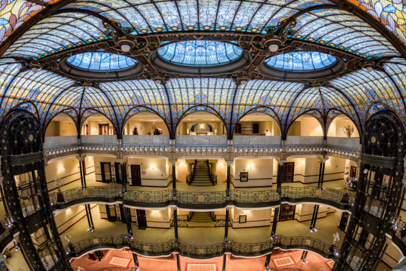 Wide-angle view of Gran Hotel Ciudad de Mexico atrium showing three oval skylights and curved wrought-iron balconies framing the space