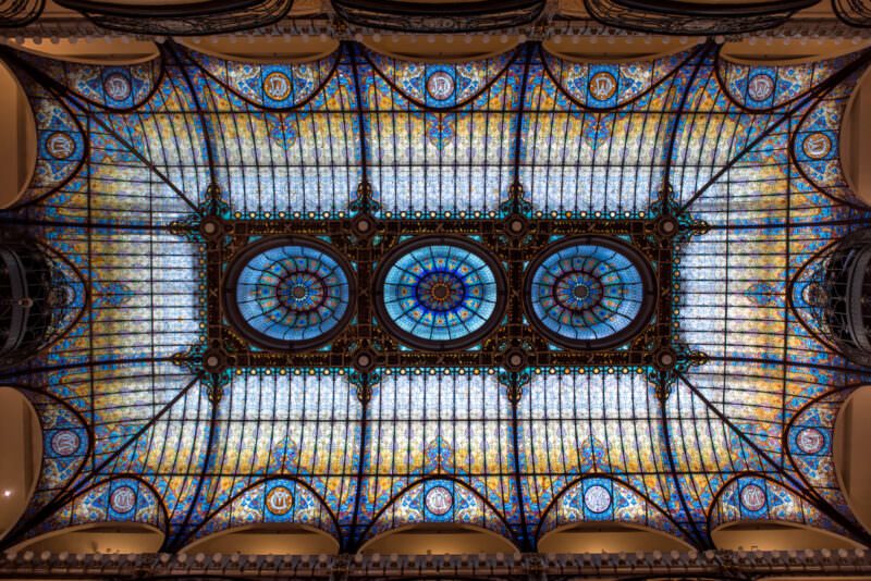 Symmetrical overhead view of Gran Hotel Ciudad de Mexico stained glass ceiling displaying three circular medallions flanked by amber glass