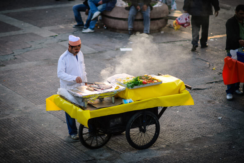 Street vendor grills fish fillets on a mobile cart to make balık ekmek near the Karaköy waterfront
