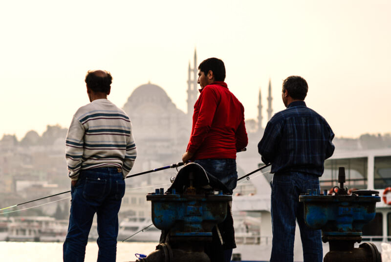 Fishermen casting lines from Karaköy's waterfront with the Süleymaniye Mosque silhouette across the Golden Horn
