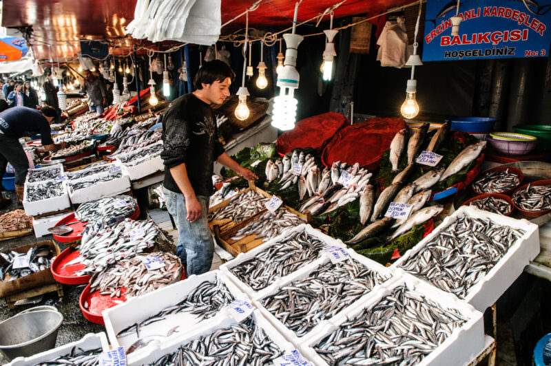 Vendor arranging crates of hamsi and iced fish under bare bulbs at Karaköy Fish Market's stalls