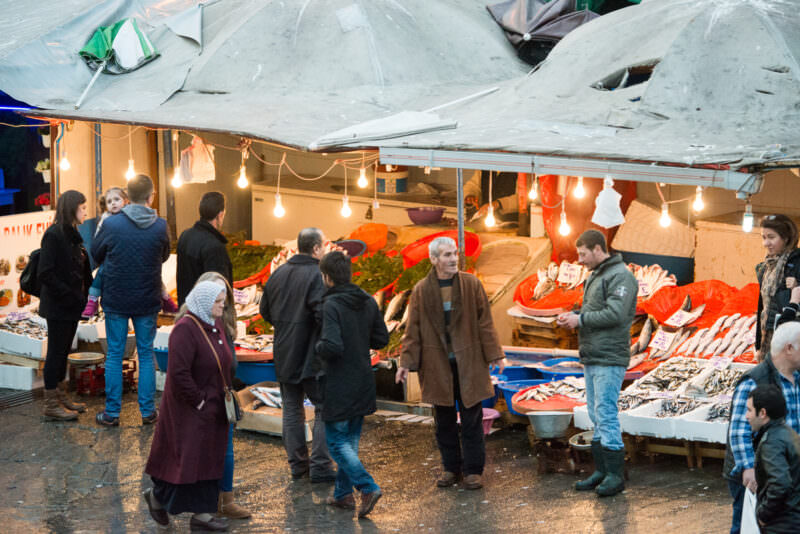 Shoppers browsing fish stalls under tarps at the rain-slicked Karaköy Balık Pazarı