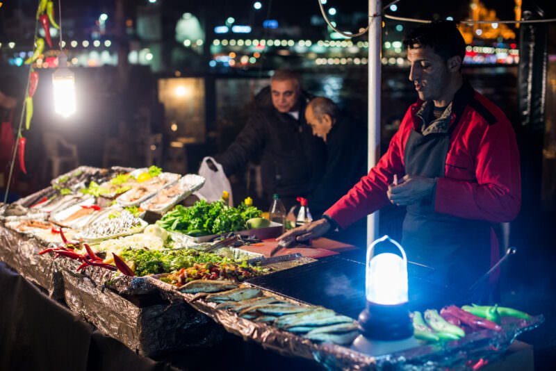 Vendor grilling fish and vegetables at a lantern-lit night stall on the Karaköy waterfront