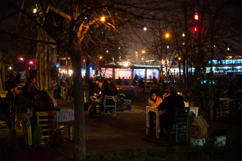 Outdoor diners sit among bare trees at a nighttime Karaköy waterfront restaurant strung with colored lights