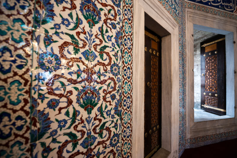 Coral-red Iznik floral tiled corridor leading to a wooden door inside the Tomb of Sultan Murad III