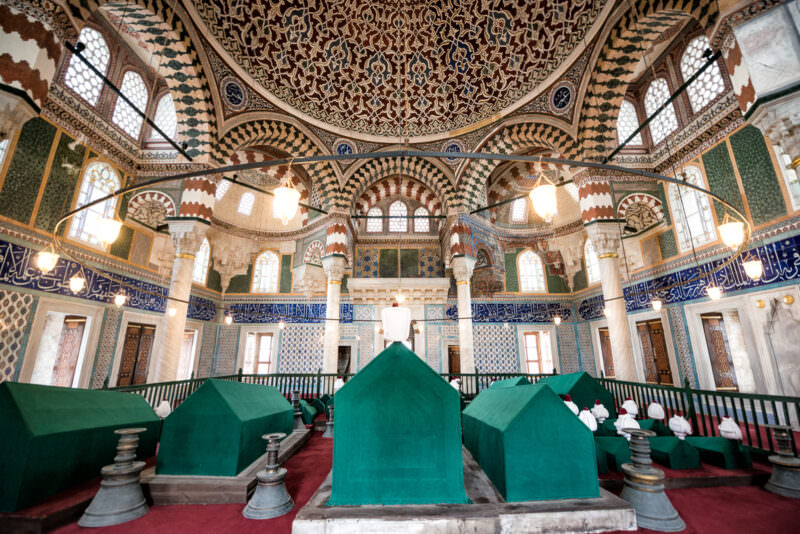 Green cloth-draped sarcophagi lined up beneath an ornate tiled dome inside the Tomb of Sultan Selim II