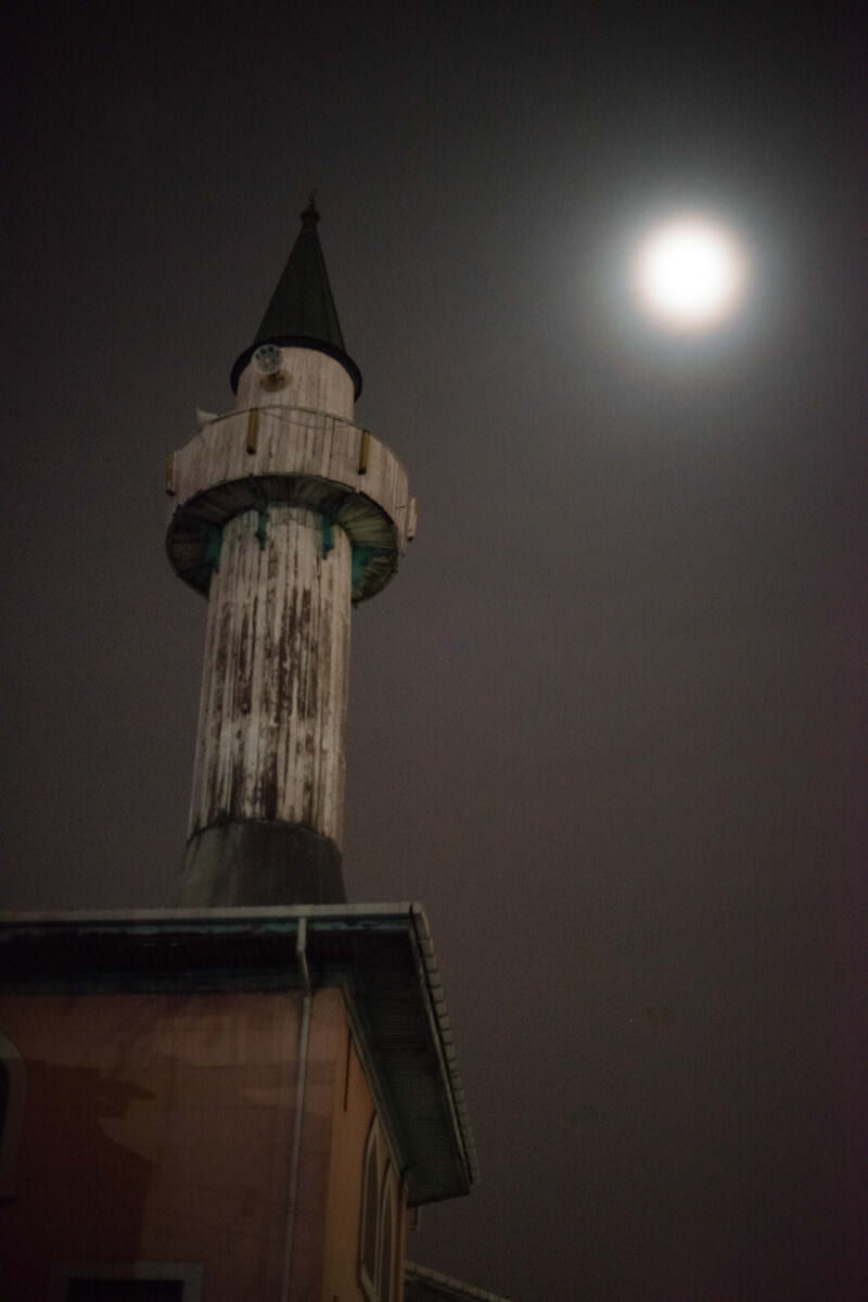 A mosque minaret silhouetted against a misty moon over the Karaköy waterfront district
