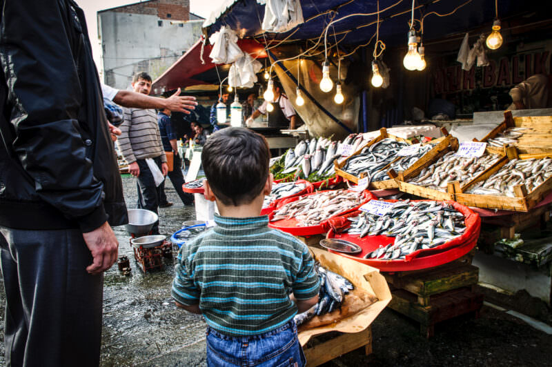 A boy stands before crates of iced fish at the Karaköy Fish Market under strings of bare bulbs