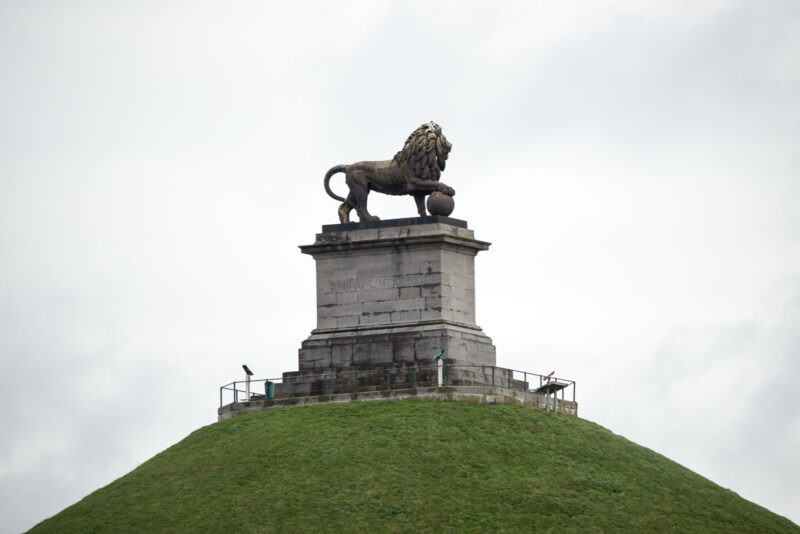 Lion's Mound with lion statue atop stone pedestal, viewed from ground level against overcast sky