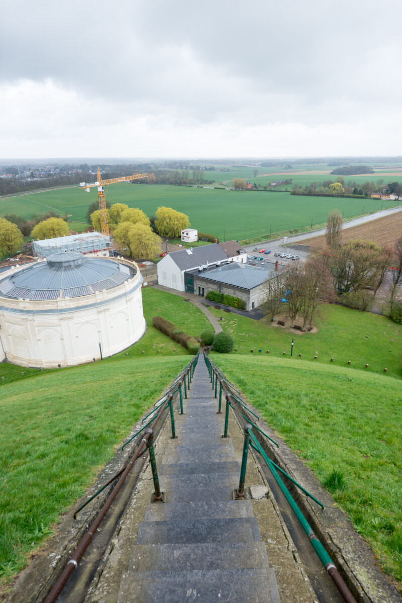 Steep staircase descending the Lion's Mound, with panoramic views of fields and a white rotunda building below