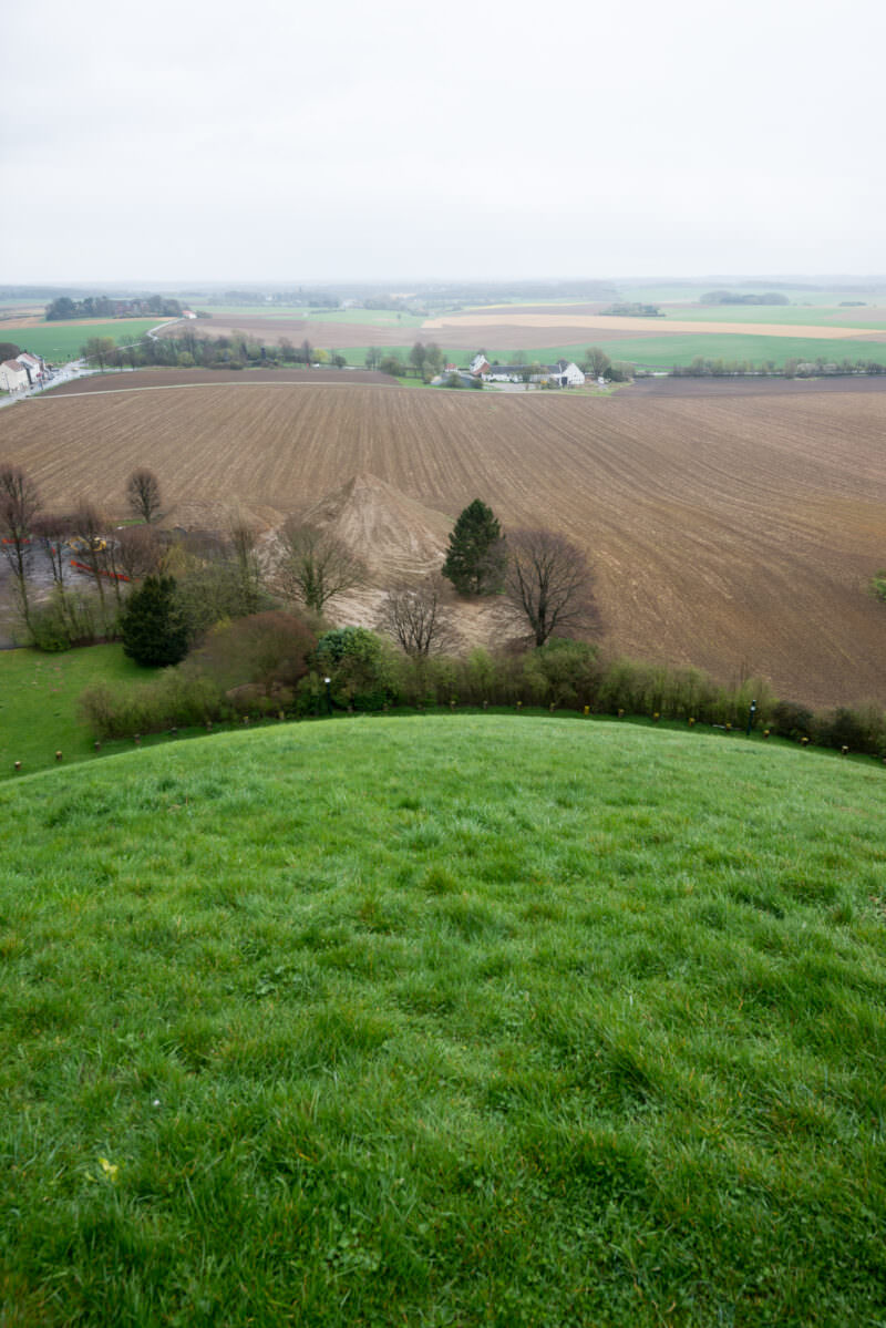 Panoramic view from the Lion's Mound summit showing patchwork fields, plowed earth, and distant villages under overcast sky