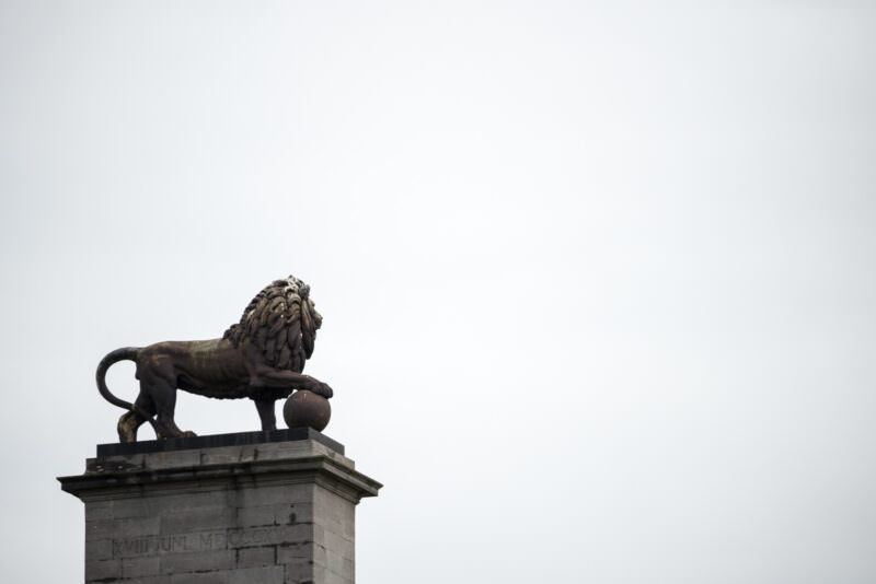 Cast-iron lion statue with flowing mane atop the Lion's Mound pedestal, viewed from below against white sky