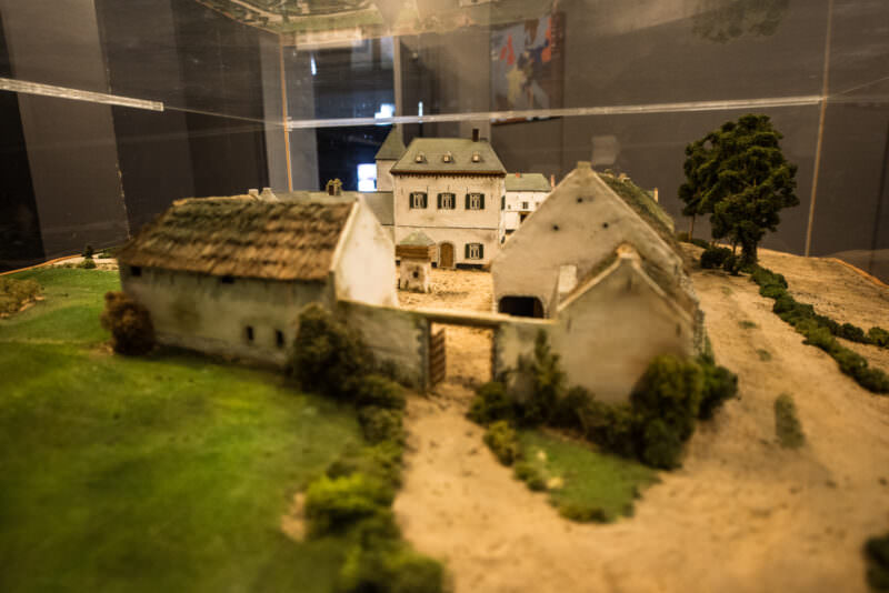 Scale model of a walled Brabantine farm with courtyard, white buildings, and miniature trees under glass