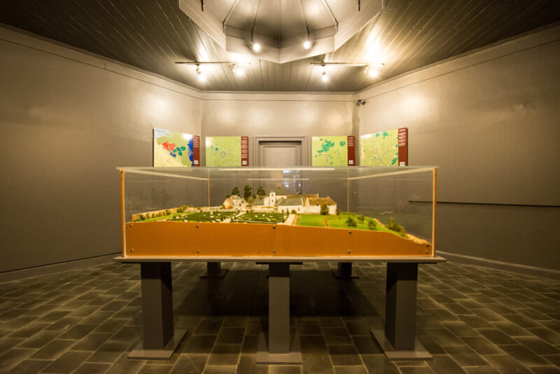 Glass-enclosed scale diorama of Château d'Hougoumont on table, with maps on walls and domed ceiling above