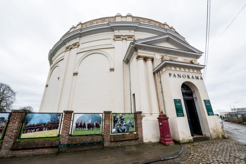 White cylindrical Panorama building with classical pediment and pilasters, viewed from the Lion's Mound base on a wet day