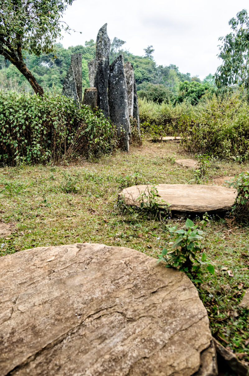 Hintang site with large flat stone disks in the foreground and jagged, lichen-covered menhirs rising behind against green hills