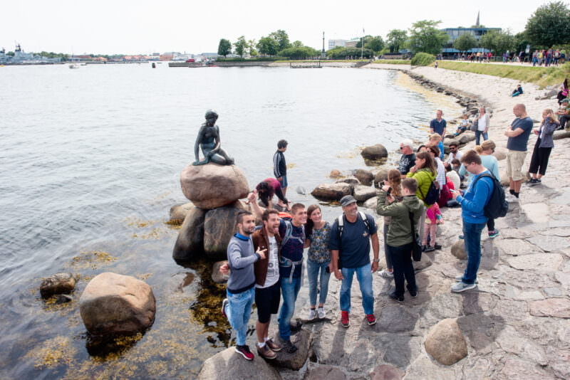 The Little Mermaid statue at Langelinie Promenade with tourists lined along the waterfront promenade and harbour beyond