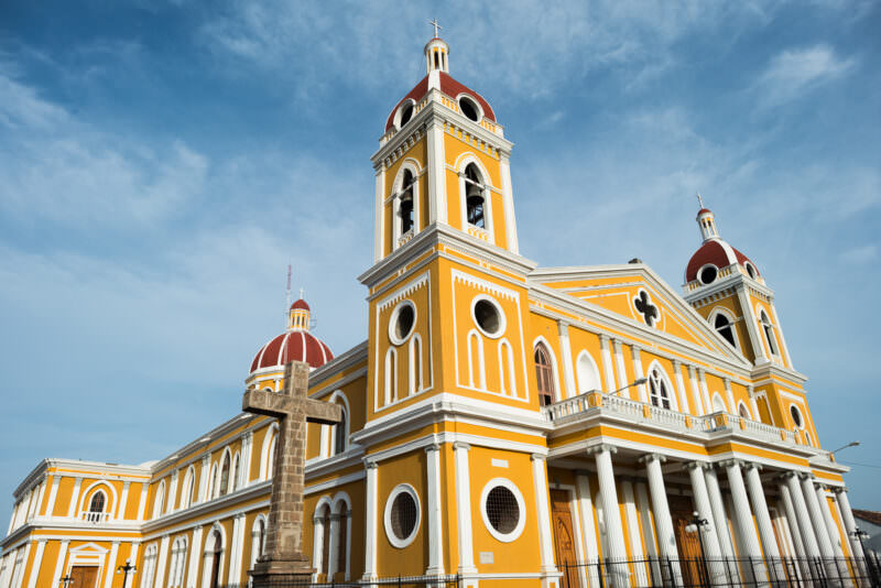 Cathedral of Granada with yellow and white facade, red dome, and twin bell towers under blue sky