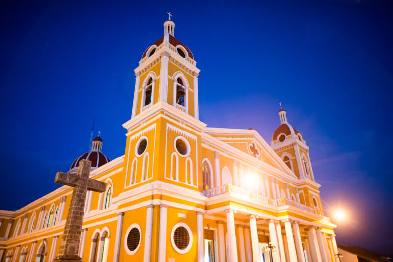 Cathedral of Granada illuminated at twilight with a carved basalt cross in the foreground