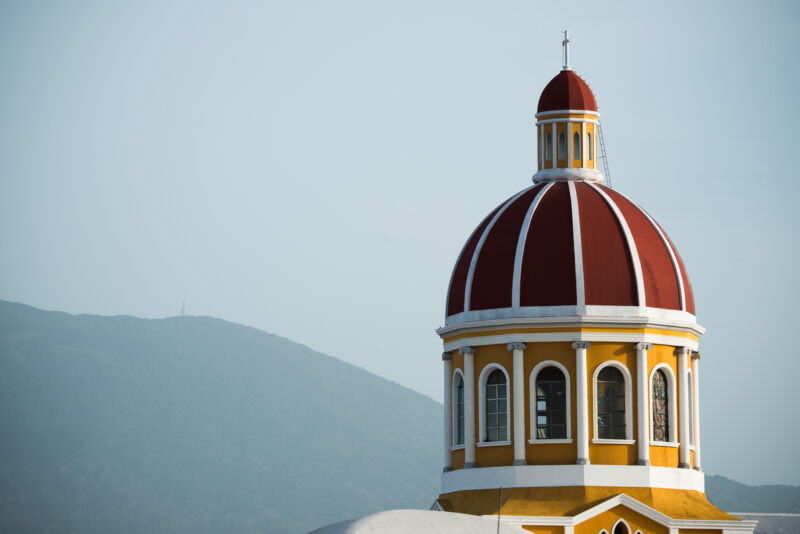 Cathedral of Granada's red dome with yellow drum and white trim, Mombacho volcano visible in background
