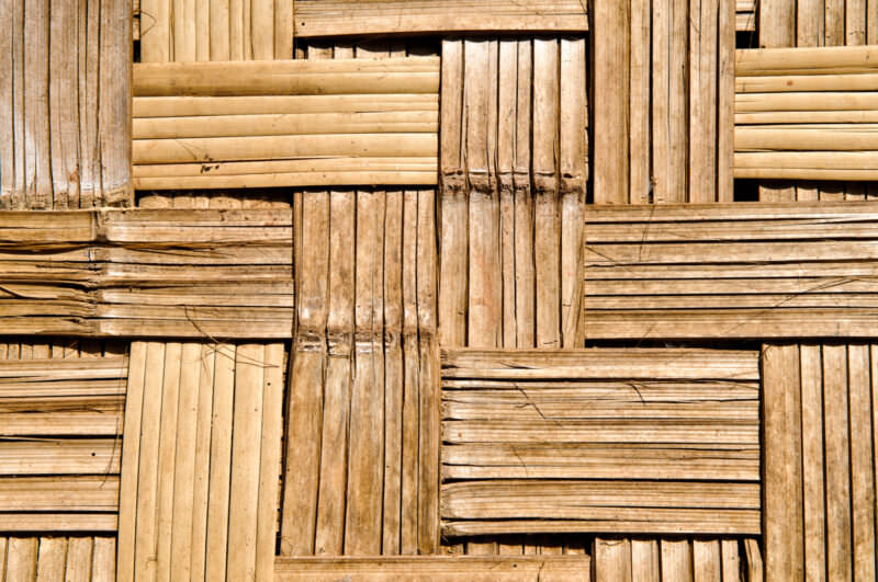 Close-up of flattened bamboo strips woven into a lattice wall panel, showing alternating horizontal and vertical weave pattern