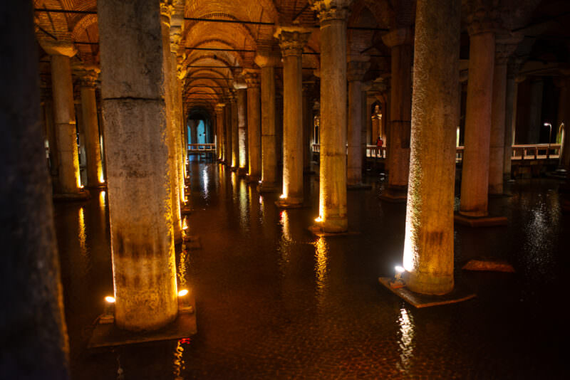 Wooden walkway winding between illuminated marble columns rising from the Basilica Cistern's water