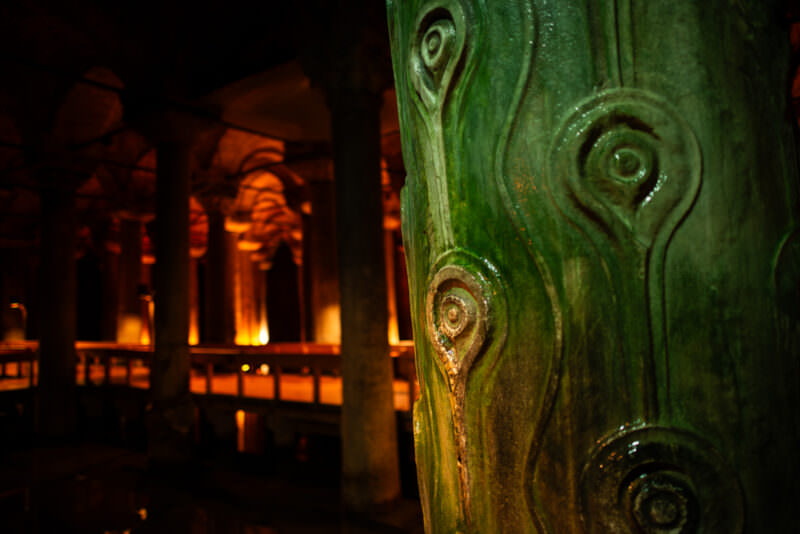 Close-up of a carved stone column with swirling patterns inside the dim Basilica Cistern