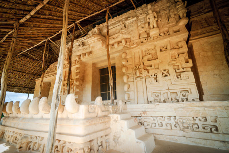 Wide view of the Sak Xok Naah at Ek' Balam under its palapa shelter, showing monster-mouth jaw and layered frieze