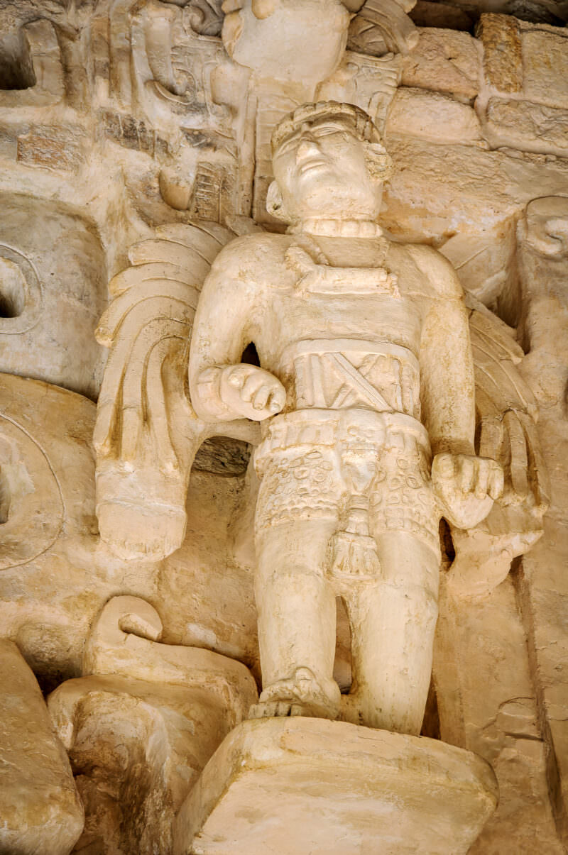 Winged stucco figure with feathered back-rack and ceremonial belt flanking the Sak Xok Naah doorway at Ek' Balam