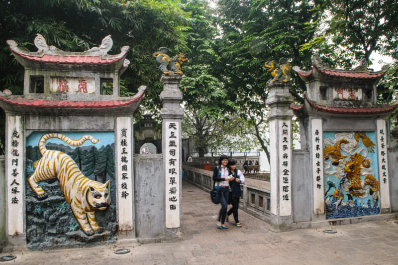 Visitors walking through Ngoc Son Temple's gate flanked by tiger and dragon relief carvings