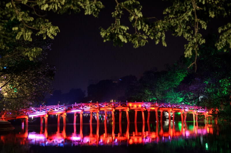 Red-lit arches of The Huc Bridge mirrored across the dark surface of Hoan Kiem Lake