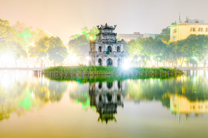 Turtle Tower on Hoan Kiem Lake reflected in still water on a foggy Hanoi night