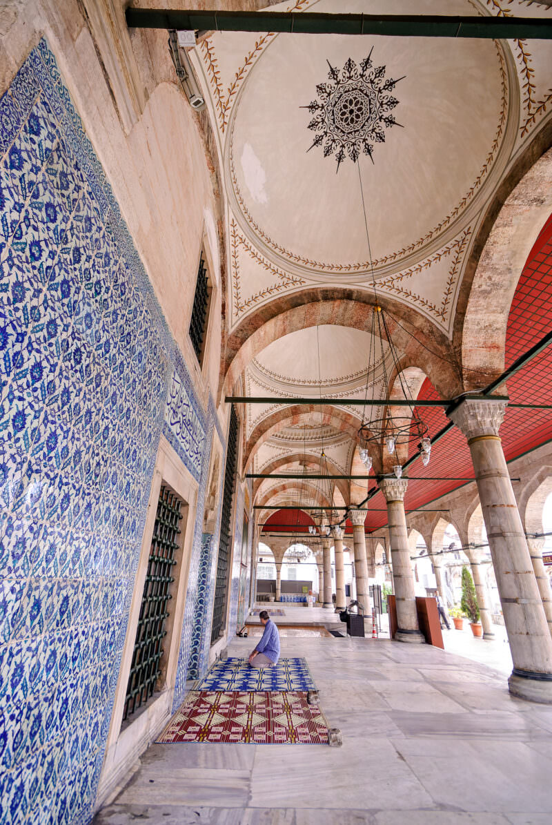 Lone worshipper kneeling on a prayer rug beneath the painted dome of Rustem Pasha Mosque's tiled entrance porch